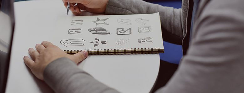 A man drawing some logos on a book with a pencil.